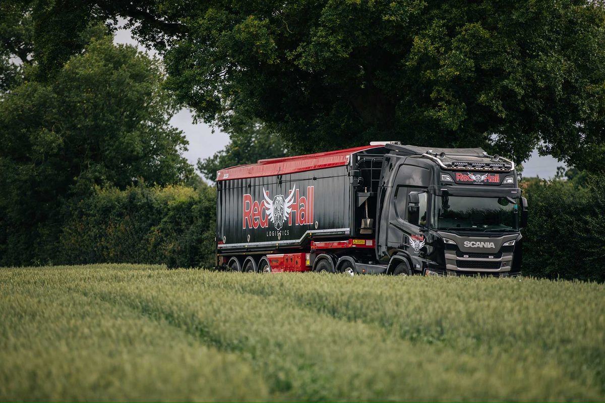 Red Hall Logistics bulk feed lorry with Muldoon blowing system driving past a wheat field